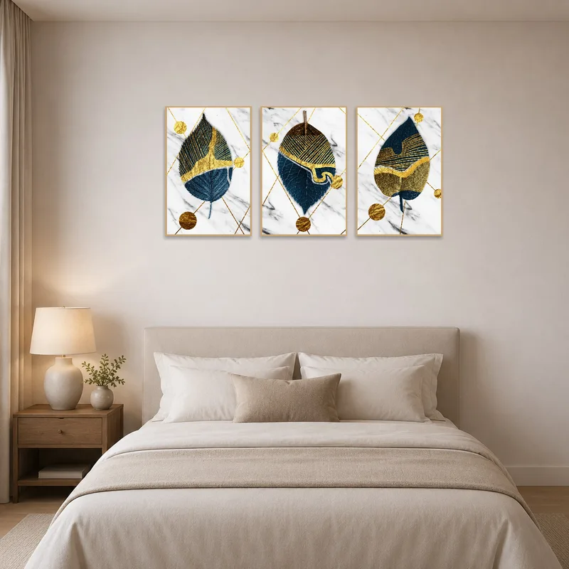 Triptych art with abstract leaf and gold patterns above a bed.