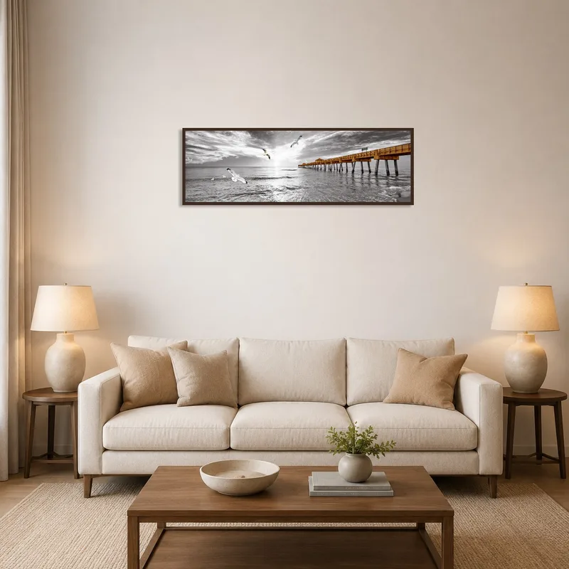 Seaside pier print on a living room wall above a modern sofa setting.